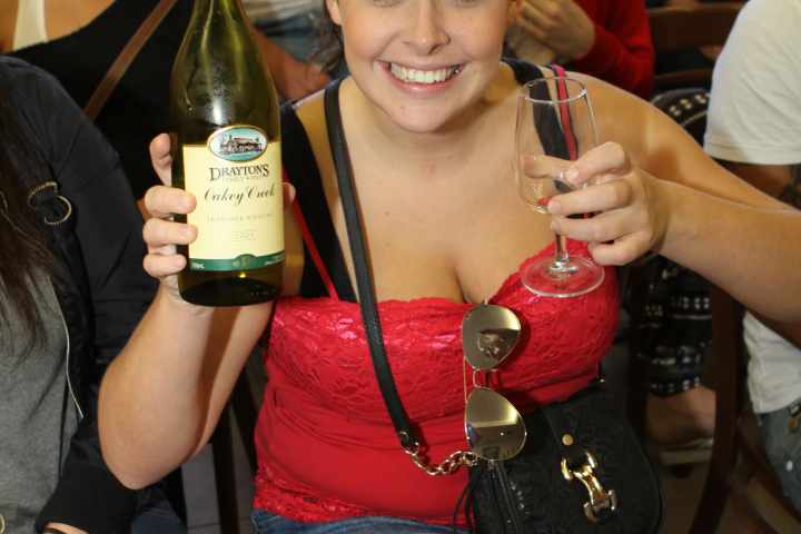 A woman holding up a bottle and her glass of wine.